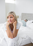 Tensed mature woman sitting in bed with man in background