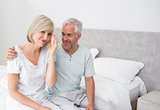 Smiling man and woman sitting on bed