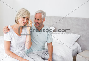 Smiling man and woman sitting on bed