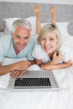 Relaxed mature couple using laptop in bed