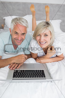 Relaxed mature couple using laptop in bed