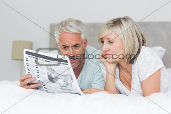 Mature couple reading newspaper in bed