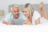 Smiling couple using digital tablet in bed