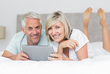 Smiling couple using digital tablet in bed