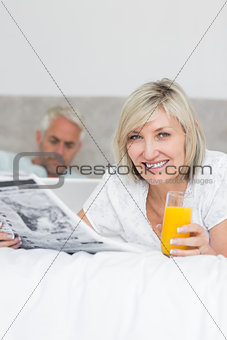 Couple reading newspaper and using laptop in bed