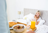 Happy woman sitting in bed with breakfast in foreground