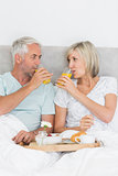 Happy mature couple having breakfast in bed