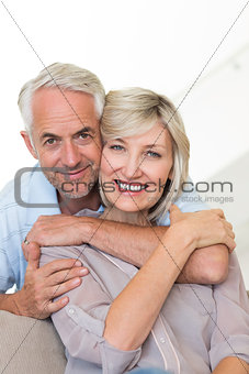 Smiling man embracing woman from behind on sofa