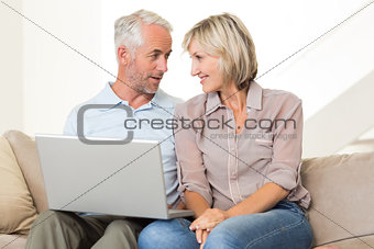 Happy mature couple using laptop on sofa