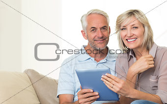 Smiling mature couple using digital tablet on sofa