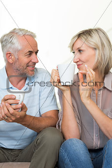 Smiling mature couple with coffee cups sitting on sofa