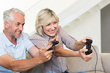 Cheerful mature couple playing video game on sofa
