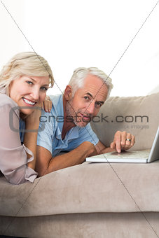 Happy mature couple using laptop on sofa