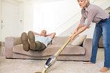 Man resting on couch while woman vacuuming area rug