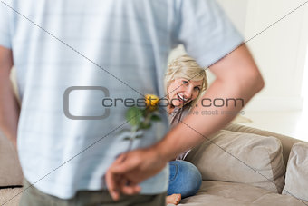 Man holding flower behind back with woman sitting on couch