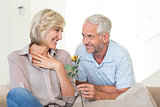 Man giving flower to a smiling woman sitting on couch