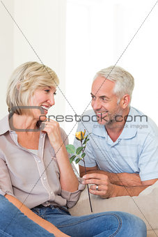 Man giving flower to a smiling woman sitting on couch