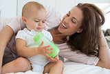 Mother with baby holding milk bottle on bed