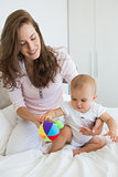 Mother and baby sitting with toy on bed