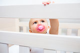 Cute baby with pacifier in mouth in the crib
