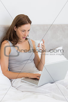Woman using laptop while having coffee in bed