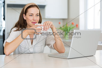 Thoughtful woman with coffee cup and laptop in kitchen