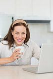 Smiling woman with coffee cup and laptop in kitchen