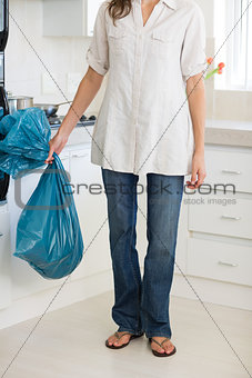 Low section of woman carrying garbage bag in kitchen