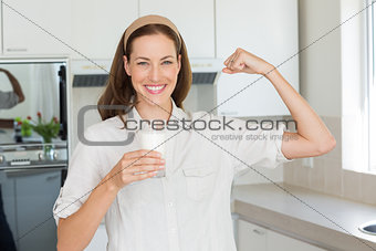 Happy woman flexing muscles while drinking water in kitchen