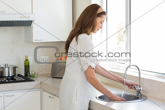 Woman washing glass at washbasin in kitchen