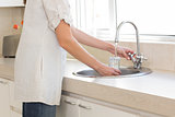 Mid section of a woman washing glass at washbasin in kitchen