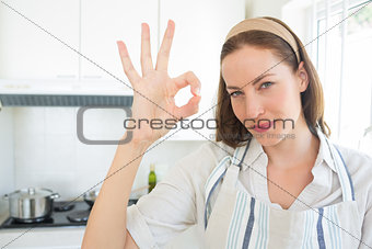 Smiling young woman gesturing okay sign in kitchen