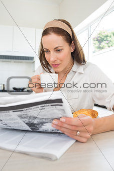 Woman with coffee cup reading newspaper in kitchen