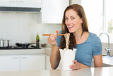 Smiling woman eating noodles in kitchen