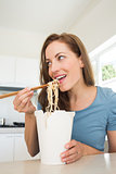 Smiling young woman eating noodles in kitchen