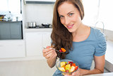 Smiling young woman eating fruit salad in kitchen