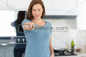 Smiling young woman holding out knife in kitchen