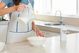Mid section of woman pouring milk into dough at kitchen