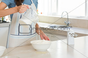 Mid section of woman pouring milk into dough at kitchen