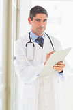 Confident male doctor writing on clipboard