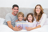 Happy family with storybook in bed