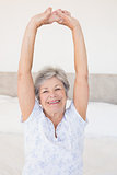 Smiling senior woman stretching on bed
