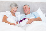 Senior man giving gift box to wife in bed