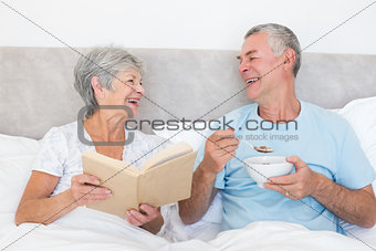 Happy couple with book and bowl in bed