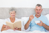 Senior couple with book and cereal bowl in bed
