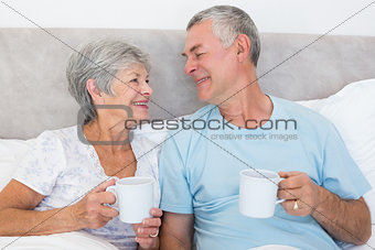 Senior couple with coffee cups in bed