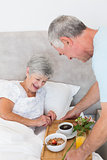 Senior man giving breakfast tray to wife in bed