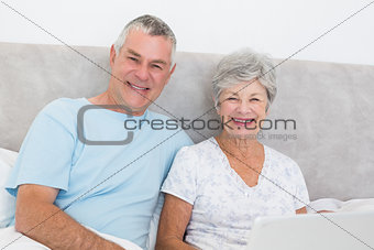 Senior couple with laptop sitting in bed