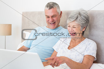 Senior couple laughing while using laptop in bed