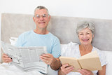 Senior couple holding newspaper and book in bed